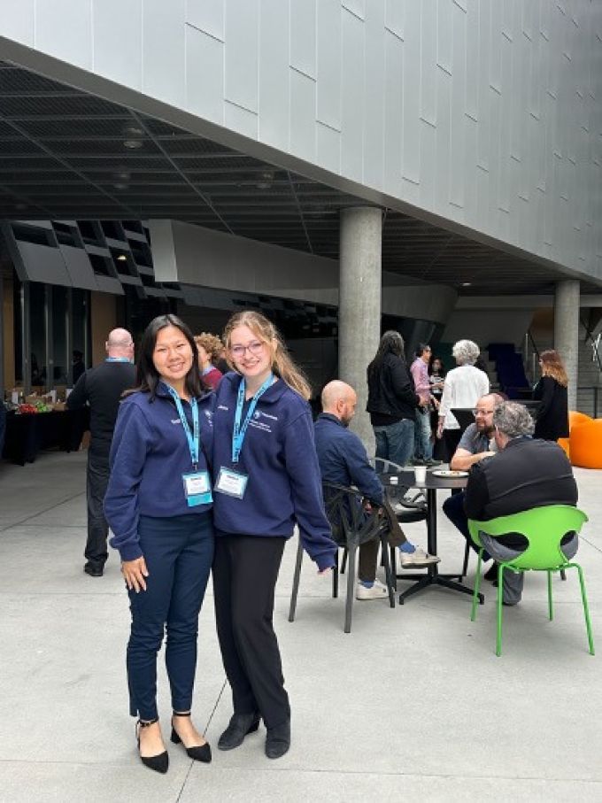 two women dressed similarly with lanyard badges inside a large room.
