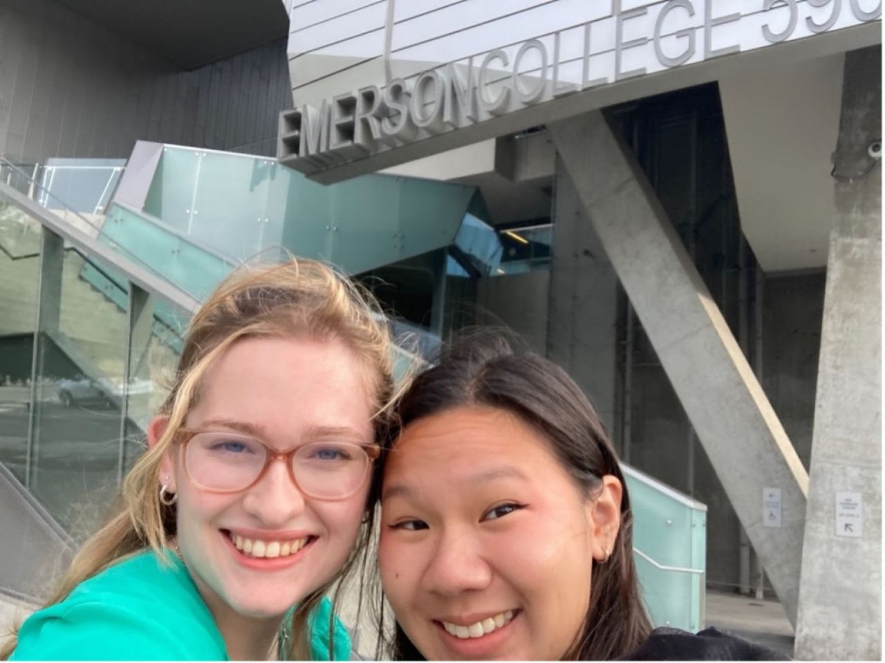 selfie photo of two women from chin up inside a building with a sign "Emerson College"