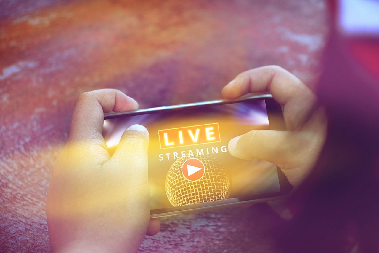 Hands holding phone in landscape orientation with "Live Steaming" on screen.