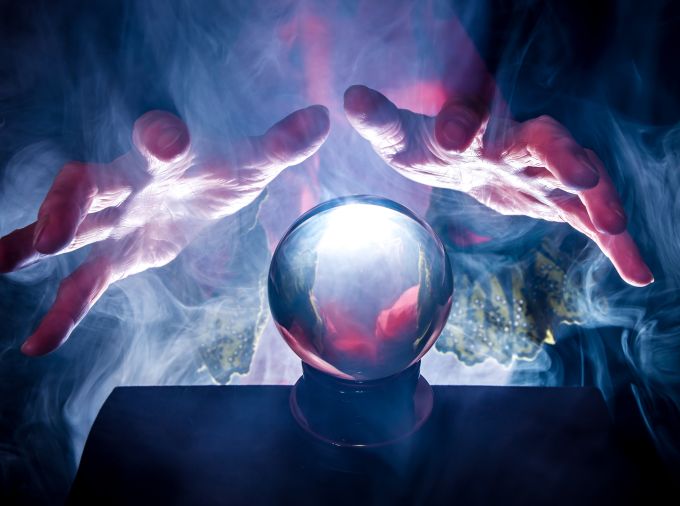 hands hover above a crystal ball in foggy, eerie lighting