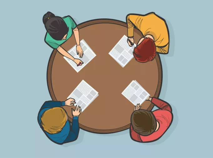 birdseye view of four people seated at circular table with letter-sized paper on the tabletop in front of each person.