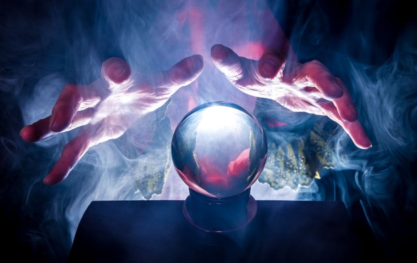 hands hover above a crystal ball in foggy, eerie lighting